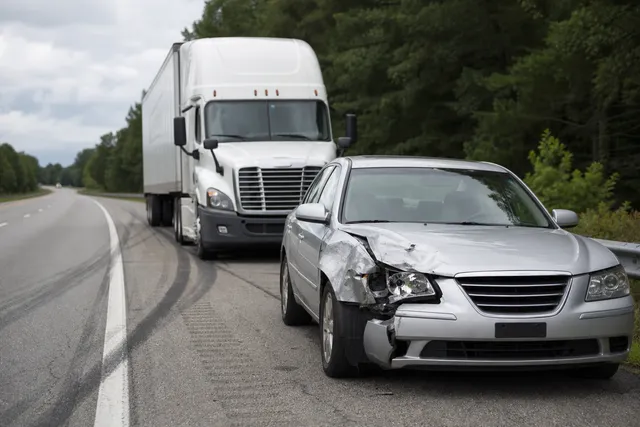 Damaged car with a tractor trailer behind it